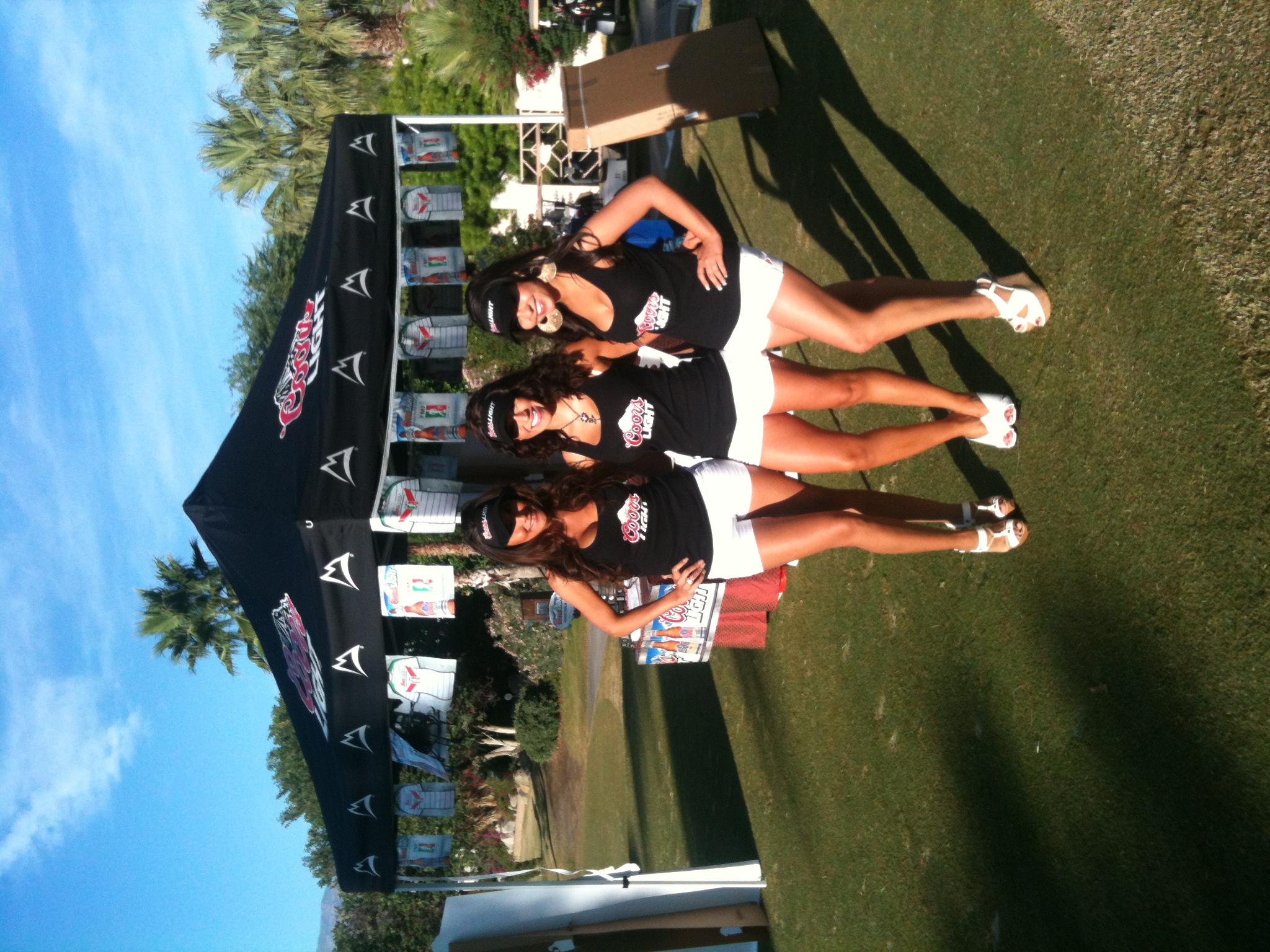 Three professional Coors Light promotional staff at upscale golf event with branded tent and displays